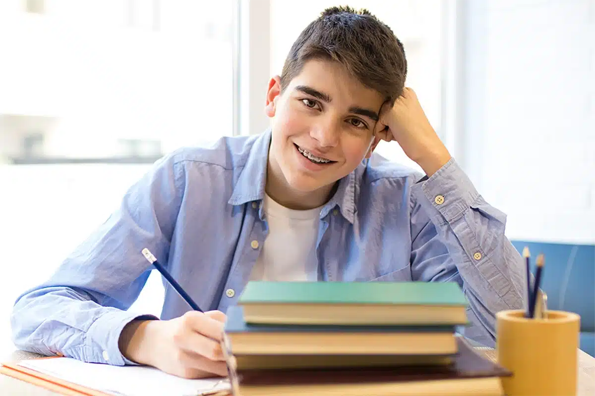 Young male student studying at desk with books and stationery.